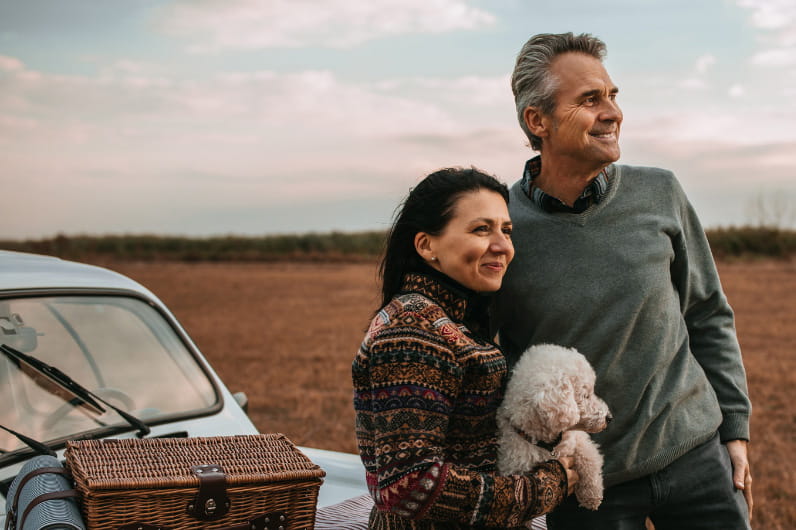 Couple with dog on picnic, standing by their car, looking off into the distance