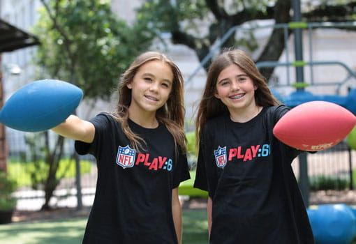 Two girls holding footballs outside