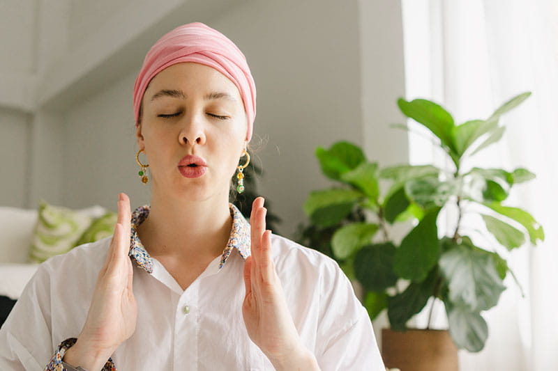 Woman with eyes closed doing breathing exercise in living room at home