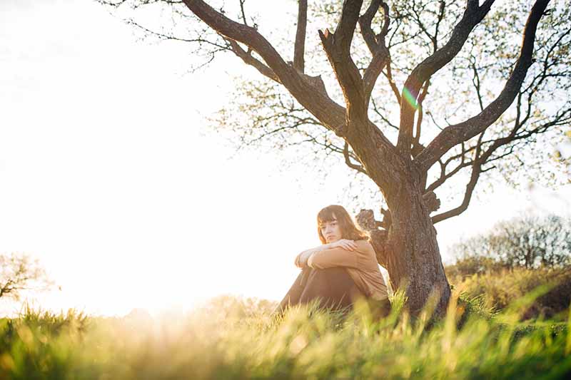 Woman sitting in front of a tree in a field