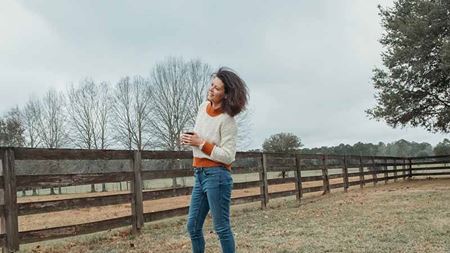 Woman standing in a field by a wooden fence