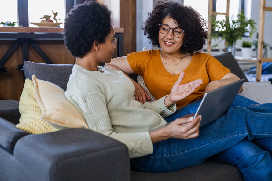 Two women chatting on couch with laptop