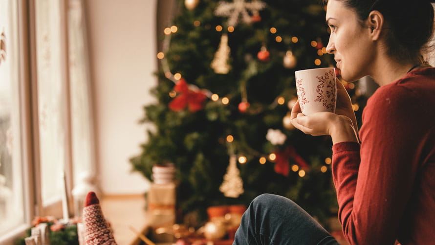 Young woman drinking tea by the Christmas tree.