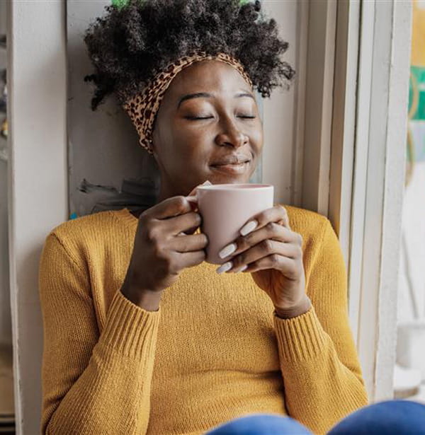 Young woman sitting by a window drinking a cup of coffee.